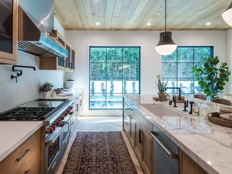 Modern kitchen with marble countertops, stainless steel appliances, wooden cabinets, and a large window overlooking greenery, perfect for real estate sellers showcasing property features.