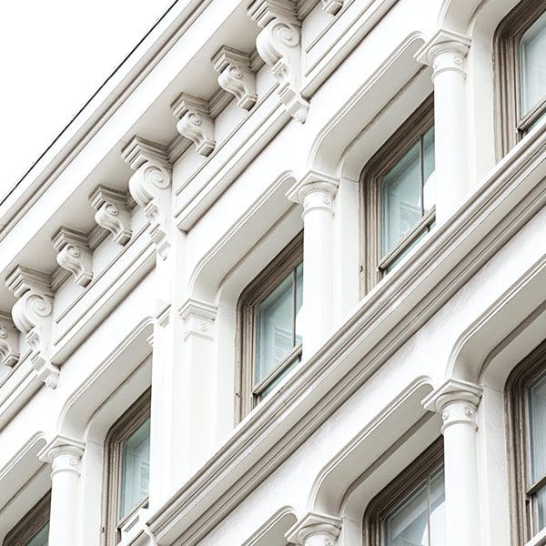 Close-up of a white neoclassical building facade, ideal for real estate sellers, with detailed cornices and arched windows.