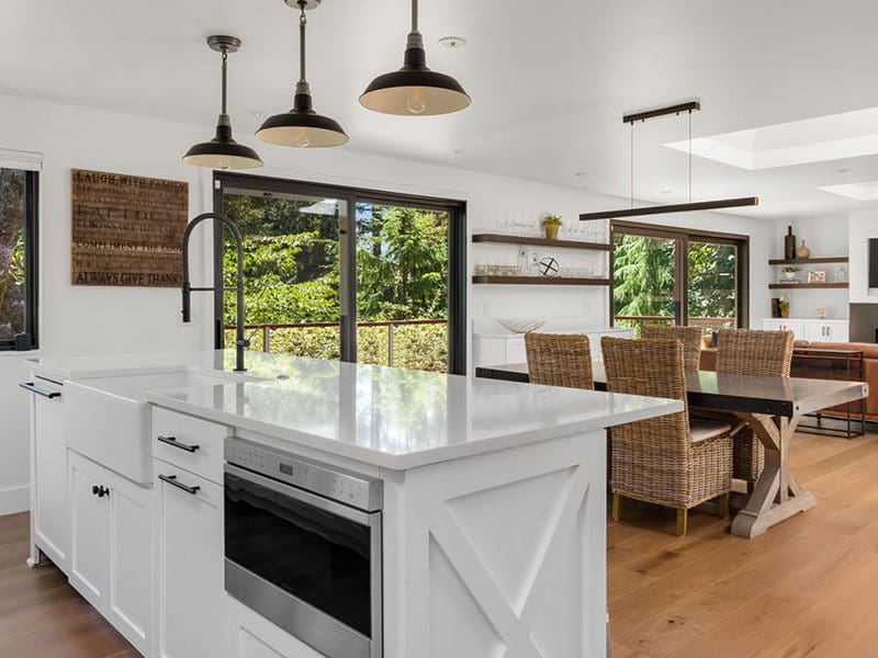 A modern kitchen with white cabinetry, a central island, and pendant lights, featuring wicker chairs and appealing to real estate buyers with a view of greenery outside.