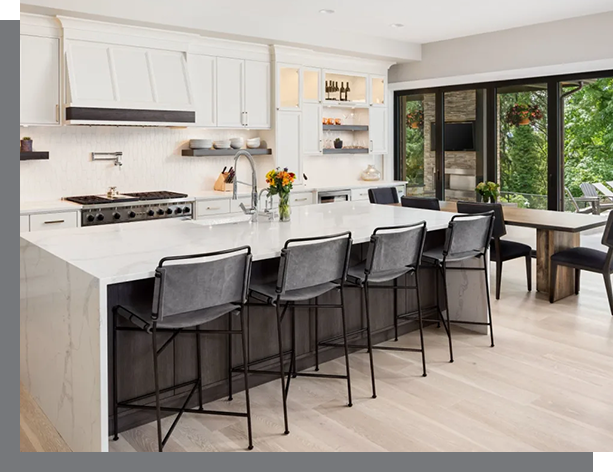 Modern kitchen interior with white cabinetry, a large island with black chairs, and a dining area by large windows overlooking greenery, designed with professional real estate services in mind.