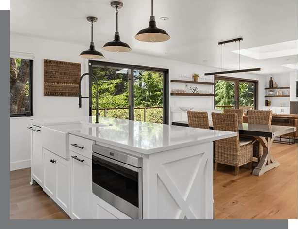 Modern kitchen with white cabinetry, a central island with a sink, pendant lights, and a dining area with wicker chairs, ideal for real estate sellers.
