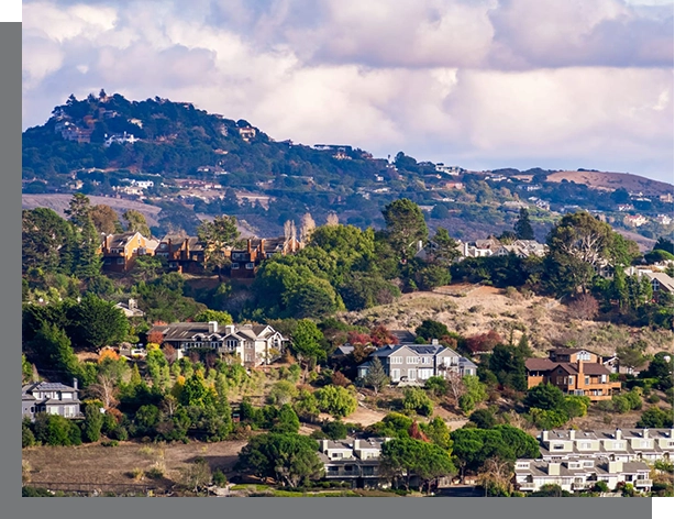 Scenic view of Mill Valley Real Estate with various houses scattered across a hilly landscape, under a cloudy sky.