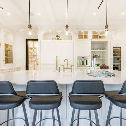 Modern kitchen interior designed for real estate buyers with white cabinetry, a central island with grey stools, and pendant lighting.